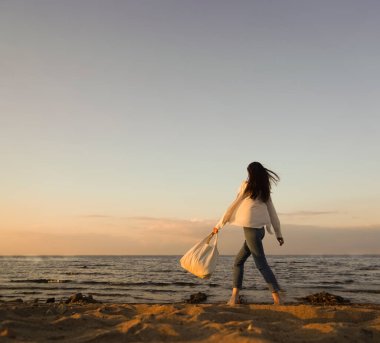 Rüzgarlı saçlı ve çantalı şık bir kadın kumlu sahilden denize yürüyor, tasasız bir an. Beyaz gömlekli şık bir bayan tatilin tadını çıkarıyor ve sahilde dinleniyor. Boşluğu kopyala