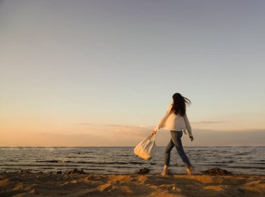 Rüzgarlı saçlı ve çantalı şık bir kadın kumlu sahilden denize yürüyor, tasasız bir an. Beyaz gömlekli şık bir bayan tatilin tadını çıkarıyor ve sahilde dinleniyor. Boşluğu kopyala
