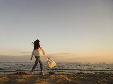 Rüzgarlı saçlı ve çantalı şık bir kadın kumlu sahilden denize yürüyor, tasasız bir an. Beyaz gömlekli şık bir bayan tatilin tadını çıkarıyor ve sahilde dinleniyor. Boşluğu kopyala