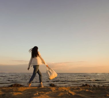 Rüzgarlı saçlı ve çantalı şık bir kadın kumlu sahilden denize yürüyor, tasasız bir an. Beyaz gömlekli şık bir bayan tatilin tadını çıkarıyor ve sahilde dinleniyor. Boşluğu kopyala