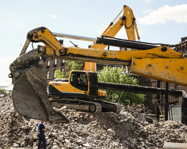 yellow  excavator loading a dump truck with debris and trash after building demolition