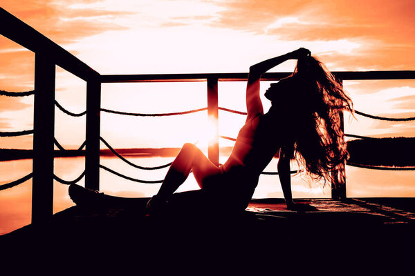 Happy woman sitting on seashore. hand raised to heaven. sunny sky light. Lady girl enjoy sunny sunset sea. Concept of freedom. Brunette long hair fluttering fly wind.