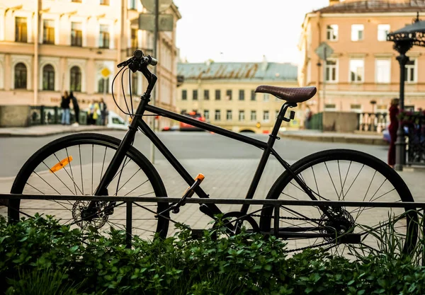 金属製のフェンスに黒いレトロな自転車が停まっていた 街の背景 市内にロックパーキング付きのヴィンテージスタイルの自転車 — ストック写真