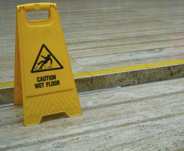 Yerlerin ıslandığına dair uyarı işareti. Döşemede sarı, ıslak bir tabela var..