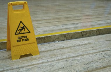 Yerlerin ıslandığına dair uyarı işareti. Döşemede sarı, ıslak bir tabela var..