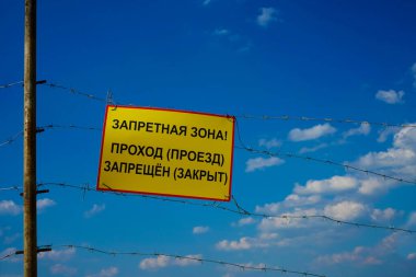 Yasak bölge. Geçiş yok. Tehlike uyarısı işareti. Bu sınırın ötesine geçemezsin. Tehlike bölgesi. Mavi gökyüzü ve beyaz bulutlar. Dikenli tel.