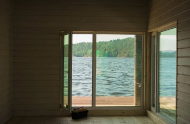 Balkonun içerisindeki odanın penceresinden balkon ve arka planda ahşap panjurlarla deniz yaz güneşli sabahıyla birlikte mavi gökyüzü görünüyor. Kimse..
