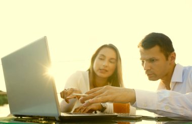 Genç çift masada oturuyor ve sorunlarını çözüyorlar. İşadamı iş kadınına bilgisayarda yeni seçenekler gösteriyor.