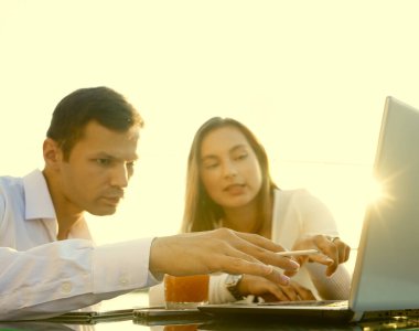 Genç çift masada oturuyor ve sorunlarını çözüyorlar. İşadamı iş kadınına bilgisayarda yeni seçenekler gösteriyor.