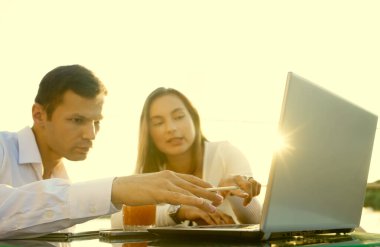 Genç çift masada oturuyor ve sorunlarını çözüyorlar. İşadamı iş kadınına bilgisayarda yeni seçenekler gösteriyor.