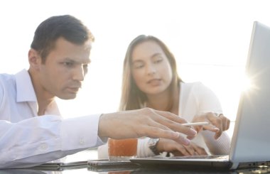 Genç çift masada oturuyor ve sorunlarını çözüyorlar. İşadamı iş kadınına bilgisayarda yeni seçenekler gösteriyor.