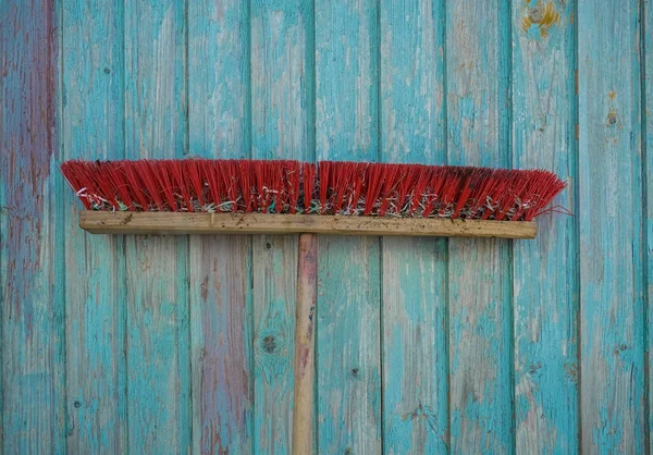 青い木製のフェンスの背景に隔離された長い木製のハンドルを持つほこりの多いブルーム 家事のための洗浄装置 プラスチック製の毛ブラシ — ストック写真