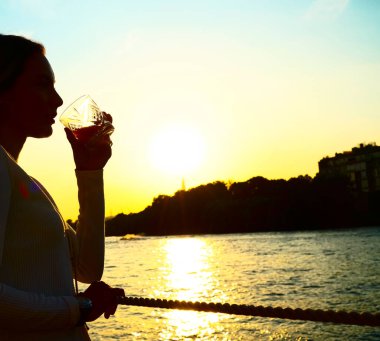 Gün batımında bardaktan portakal suyu içen bir kadının silüet fotoğrafı. .
