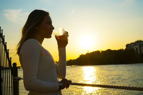 夕暮れ時にガラスからオレンジジュースを飲む女性のシルエット — ストック写真