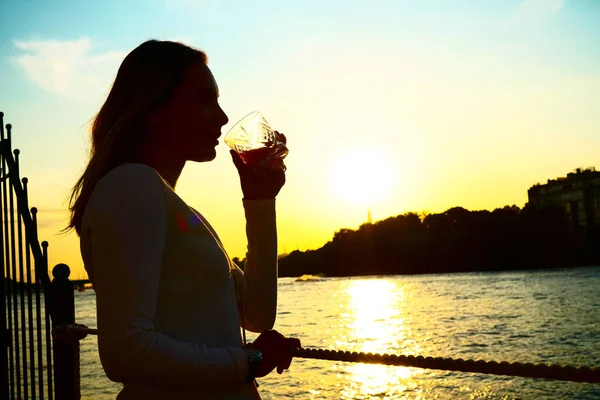 夕暮れ時にガラスからオレンジジュースを飲む女性のシルエット — ストック写真