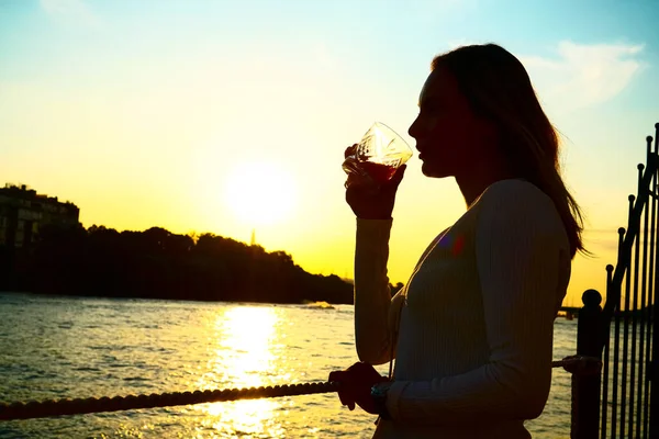 夕暮れ時にガラスからオレンジジュースを飲む女性のシルエット — ストック写真