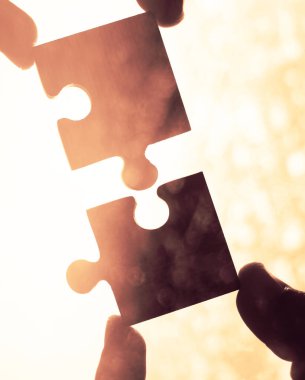 Gökyüzü arka planında yapboz parçaları olan eller.  