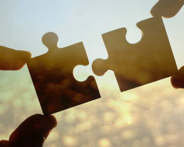 Gökyüzü arka planında yapboz parçaları olan eller.  