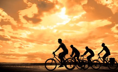 Boşluk. Gün batımında bisiklete binen sportif arkadaşlar. Bisikletçiler sahil boyunca gidiyor. Doğa arka planında spor.