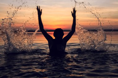 Siyah kadın silueti. Başının üstüne su sıçratıyor. Yaz tatili. tatil aktif. Deniz ve günbatımı gökyüzü. Sağlıklı mutluluk yaşam tarzı. Eller yukarı..