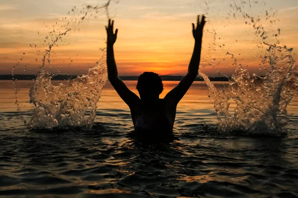 Black silhouette of woman. splashing water above head.  summer vacation. holiday active.  sea and sunset sky. Healthy happiness lifestyle. hands up.