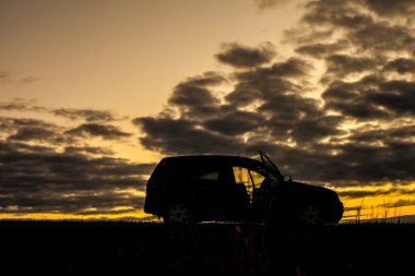 Yaz günbatımı, gökyüzündeki bir tarlada. Siyah, parlak, sarı renkli, bulutlu..