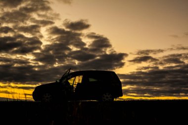 Yaz günbatımı, gökyüzündeki bir tarlada. Siyah, parlak, sarı renkli, bulutlu..