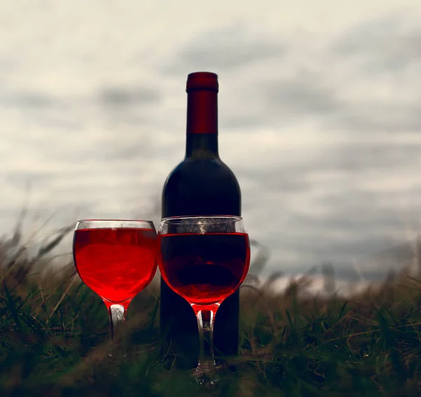 Bottle of wine and two glasses on the grass, picnic, engagement. one bottle of red wine with two glasses  on summer green grass background.