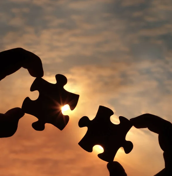 hands  with  puzzle pieces on sky background.