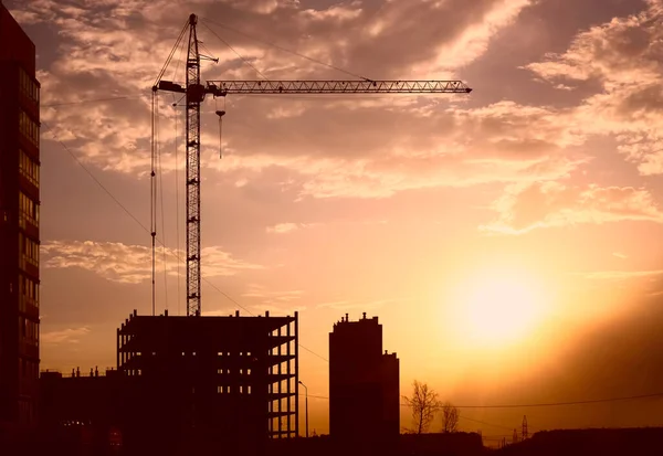 Background of silhouette building crane lift loads with sun set rays yellow cloudy evening sky backdrop Construction site at orange sunset