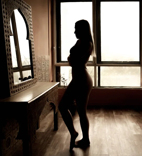 一个穿着睡衣的美丽纤细的女孩站在镜子前的照片 黑暗房间 侧视图 — 图库照片