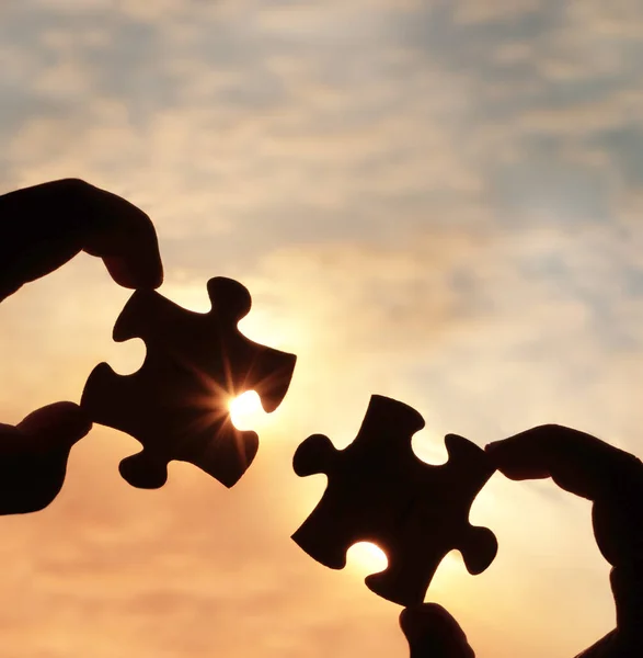 hands  with  puzzle pieces on sky background.