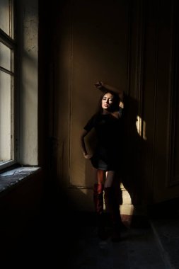 Siyah kısa elbiseli güzel orta yaşlı kadın bir duvarın yanında duruyor.