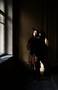 Siyah kısa elbiseli güzel orta yaşlı kadın bir duvarın yanında duruyor.