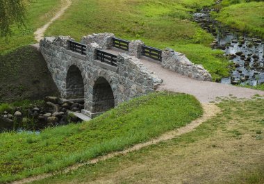 Yazın güzel nehrin üzerindeki eski taş köprü. Yeşillikler arasında parktaki eski taş kemer köprüsü. 