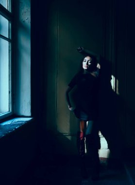 Siyah kısa elbiseli güzel orta yaşlı kadın bir duvarın yanında duruyor.