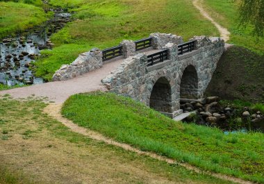 Yazın güzel nehrin üzerindeki eski taş köprü. Yeşillikler arasında parktaki eski taş kemer köprüsü. 