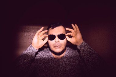 Güneş gözlüğü takan çekici bir genç adam ve örgü ören bir kazak. Kameraya bakıyorum. izole edilmiş duvar arkaplanı