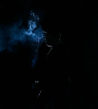 Siyah arka planda sigara içen adamın silüeti.
