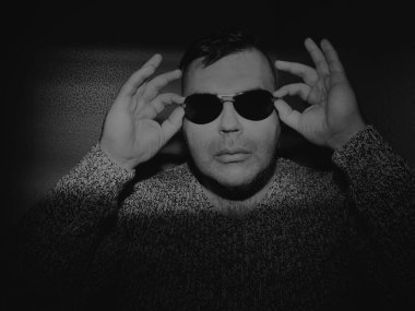 Güneş gözlüğü takan çekici bir genç adam ve örgü ören bir kazak. Kameraya bakıyorum. izole edilmiş duvar arkaplanı