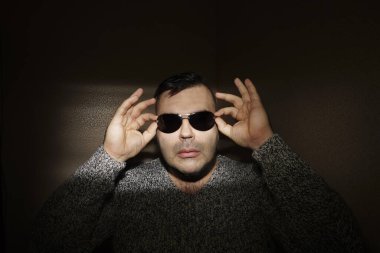 Güneş gözlüğü takan çekici bir genç adam ve örgü ören bir kazak. Kameraya bakıyorum. izole edilmiş duvar arkaplanı