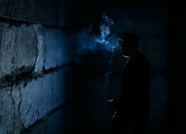 Siyah arka planda sigara içen adamın silüeti.