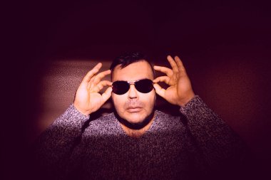 Güneş gözlüğü takan çekici bir genç adam ve örgü ören bir kazak. Kameraya bakıyorum. izole edilmiş duvar arkaplanı