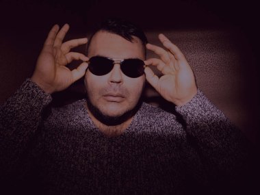 Güneş gözlüğü takan çekici bir genç adam ve örgü ören bir kazak. Kameraya bakıyorum. izole edilmiş duvar arkaplanı