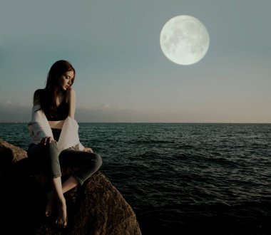 Portrait of young woman on stones near sea. Beautiful girl is resting on coast, enjoying outdoor recreation. clipart