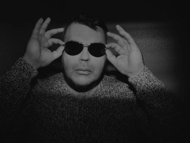 Güneş gözlüğü takan çekici bir genç adam ve örgü ören bir kazak. Kameraya bakıyorum. izole edilmiş duvar arkaplanı