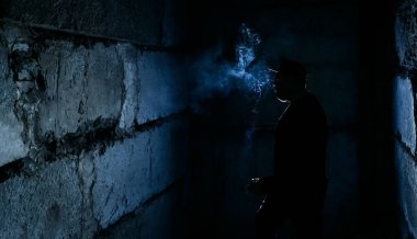 Siyah arka planda sigara içen adamın silüeti.