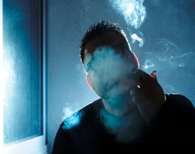 Sigara içen genç bir adamın portresi. Yakışıklı genç adam düşünceli ve sakince sigara içiyor. Erkek güzelliği, moda.