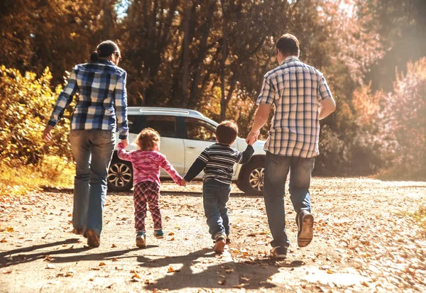 mother, father and kids - daughter, son holding hands  against white SUV big car. Outdoor photo in autumn park. Casual dress. Sunset light rays