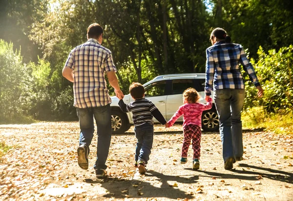 mother, father and kids - daughter, son holding hands  against white SUV big car. Outdoor photo in autumn park. Casual dress. Sunset light rays